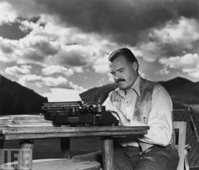 Ernest Hemingway typing at his desk outdoors.